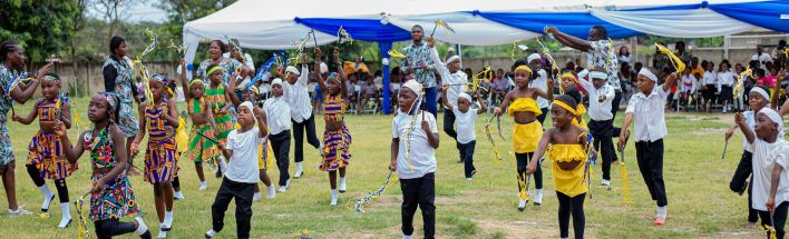 Children in traditional attire performing a lively dance at an outdoor event in Winneba, Ghana.